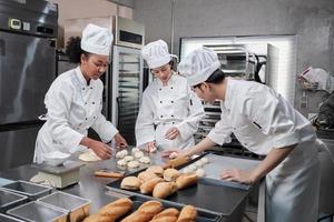 equipe de chefs em uniformes se preparam para assar pão e pastelaria na cozinha inoxidável. foto