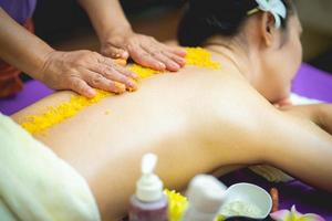 linda mulher desfrutando de uma massagem de esfoliação com sal e tendo tratamento de esfoliação na sala de spa. morena recebendo um tratamento de beleza de esfoliação com sal no spa. esfoliação corporal. foto