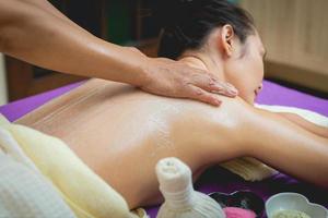 linda mulher desfrutando de uma massagem de esfoliação com sal e tendo tratamento de esfoliação na sala de spa. morena recebendo um tratamento de beleza de esfoliação com sal no spa. esfoliação corporal. foto