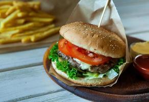 grande hambúrguer saboroso em uma mesa de madeira e batatas fritas. delicioso hambúrguer com carne, tomate, queijo e alface. foto