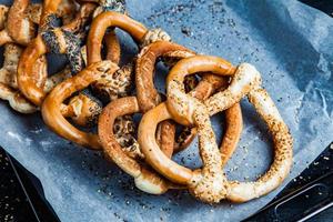 pretzels macios caseiros preparados na hora. diferentes tipos de bagels assados com sementes em um fundo preto. foto