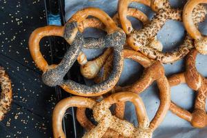 pretzels macios caseiros preparados na hora. diferentes tipos de bagels assados com sementes em um fundo preto. foto