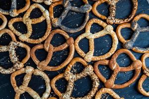 pretzels macios caseiros preparados na hora. diferentes tipos de bagels assados com sementes em um fundo preto. foto