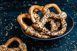 pretzels macios caseiros preparados na hora. diferentes tipos de bagels assados com sementes em um fundo preto. foto