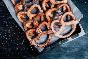 pretzels macios caseiros preparados na hora. diferentes tipos de bagels assados com sementes em um fundo preto. foto