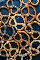 pretzels macios caseiros preparados na hora. diferentes tipos de bagels assados com sementes em um fundo preto. foto