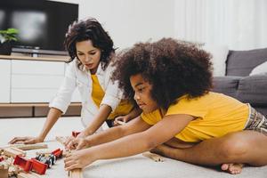 mãe solteira vivendo com duas filhas aprendendo e brincando de brinquedo de quebra-cabeça no apartamento em casa. babá olhando ou cuidando de crianças na sala de estar pessoas negras.