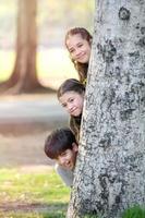 um menino meio tailandês e uma namorada mista tailandesa-europeia brincam secretamente atrás de uma grande árvore em um parque foto