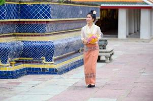 mulher tailandesa atraente em um vestido tailandês antigo segura flores frescas em homenagem ao buda para fazer um desejo no tradicional festival songkran na tailândia foto