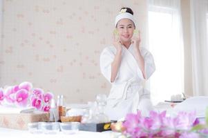 uma linda mulher asiática usa pepino para tratamento facial, juntamente com uma massagem de um massagista profissional no salão spa foto