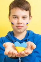 coração de cores amarelas e azuis da bandeira ucraniana nas mãos de um menino. foco variado. formato vertical foto
