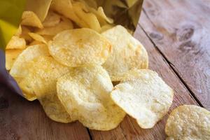 pacote aberto de deliciosas batatas fritas na mesa de madeira foto