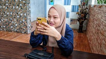 Cianjur regency, west java, indonésia em 7 de abril de 2022 - uma mulher muçulmana indonésia usando um hijab está segurando um smartphone. foto