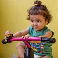 menino bonitinho shivaay dirigindo ciclo na varanda de casa durante o verão, doce garotinho sessão de fotos durante o dia, garotinho gosta de andar de bicicleta em casa durante a sessão de fotos