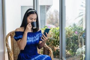 bela jovem tomando café, usando o aplicativo de celular para verificar as mídias sociais, foto