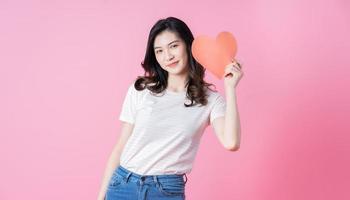 jovem garota asiática segurando a forma de coração no fundo rosa foto