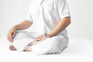 um homem de túnica branca meditando contra um pano de fundo branco com um traçado de recorte. foto