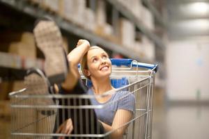 cliente de mulher alegre com sorrindo e olhando para cima enquanto está sentado no carrinho de compras na loja de ferragens foto