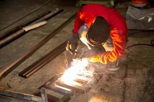 soldador usou pedra de amolar em aço na fábrica com faíscas, processo de soldagem na oficina industrial, mãos com instrumento no quadro. foto