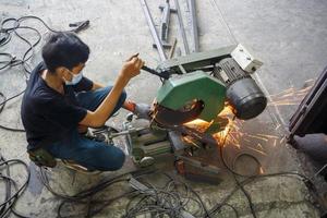 soldador usou pedra de amolar em aço na fábrica com faíscas, processo de soldagem na oficina industrial, mãos com instrumento no quadro. foto