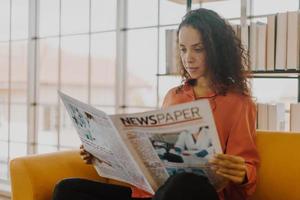 mulher da américa latina lendo jornal no sofá foto