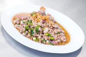 salada de carne de porco picada picante é comida tradicional do nordeste da tailândia. contém carne de porco picada, arroz torrado, pimentão assado e ervas tailandesas misturadas. foi colocado na chapa branca. foto