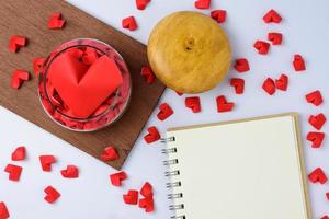 o grande coração está em uma jarra de corações com corações de papel, caderno colocado sobre a mesa. foto