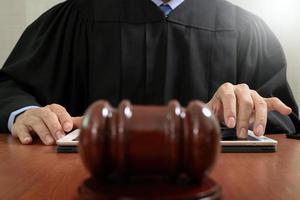 conceito de justiça e direito. juiz masculino em um tribunal batendo o martelo, trabalhando com teclado de encaixe de computador tablet digital na mesa de madeira foto
