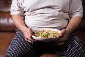 um homem gordo em vestido casual comendo salada fresca, conceito de comida saudável foto