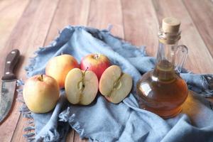 vinagre de maçã em frasco de vidro com maçã verde fresca na mesa foto