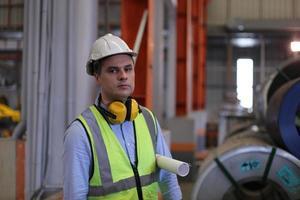 engenheiro industrial de homens usando um capacete de segurança em pé em uma fábrica industrial pesada. a manutenção procurando trabalhar em máquinas industriais e verificar a configuração do sistema de segurança na fábrica. foto