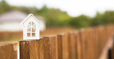 pequena figura de casa de madeira branca na cerca com chave para habitação no contexto das casas de campo. construir, projetar, projetar, mudar de casa, hipotecar, alugar e comprar imóveis. espaço de cópia foto