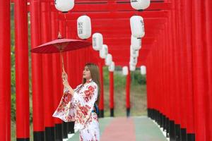 jovem garota asiática vestindo roupas tradicionais japonesas de quimono e guarda-chuva vermelho. foto