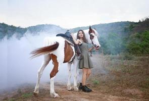 jovem e bonita com seu cavalo na luz do sol à noite. fotografia ao ar livre com garota modelo de moda. humor de estilo de vida foto