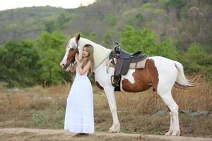 jovem e bonita com seu cavalo na luz do sol à noite. fotografia ao ar livre com garota modelo de moda. humor de estilo de vida foto