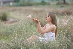 bela jovem sentada no campo na grama verde e soprando dente de leão. ao ar livre. Aproveite a natureza. menina sorridente saudável no gramado da primavera. conceito livre de alergia. liberdade foto