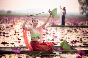 jovens mulheres asiáticas em trajes tradicionais no barco e flores de lótus rosa na lagoa foto