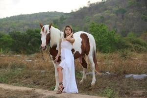 jovem e bonita com seu cavalo na luz do sol à noite. fotografia ao ar livre com garota modelo de moda. humor de estilo de vida foto