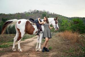 jovem e bonita com seu cavalo na luz do sol à noite. fotografia ao ar livre com garota modelo de moda. humor de estilo de vida foto