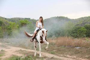 jovem e bonita com seu cavalo na luz do sol à noite. fotografia ao ar livre com garota modelo de moda. humor de estilo de vida foto