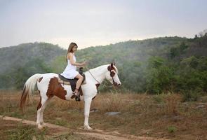 jovem e bonita com seu cavalo na luz do sol à noite. fotografia ao ar livre com garota modelo de moda. humor de estilo de vida foto