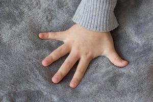 a mão da criança em um fundo cinza. a mão de uma garota com os dedos estendidos em um tecido de pelúcia cinza foto