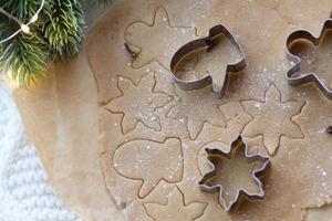 massa de gengibre enrolada em cima da mesa com cortadores de biscoito de natal e um galho de abeto. silhuetas no teste. biscoitos de natal vistos de cima foto