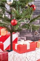 árvore de natal decorada com lindos presentes vermelhos e brancos embrulhados em casa com parede de tijolos pretos, conceito de design festivo, close-up. foto