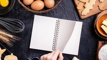 mulher está lendo a receita do livro de receitas de fazer biscoitos de halloween com ingredientes de cozimento, conceito de design de aula de culinária, vista superior, postura plana, sobrecarga. foto