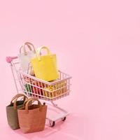 conceito de temporada de compras de venda anual - carrinho de carrinho de mini loja vermelho cheio de presente de saco de papel isolado em fundo rosa pálido, espaço de cópia em branco, close-up foto