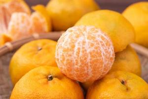 fresca, linda tangerina de cor laranja na peneira de bambu sobre a mesa de madeira escura. fruta sazonal e tradicional do ano novo lunar chinês, close-up. foto