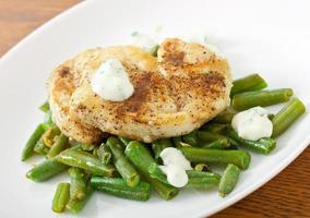 peito de frango grelhado com feijão verde e molho num prato branco. foto