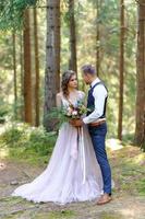 um atraente casal recém-casado, um momento feliz e alegre. um homem e uma mulher se barbeiam e se beijam com roupas de férias. cerimônia de casamento de estilo boêmio na floresta ao ar livre. foto