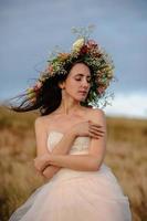 a noiva em um lindo vestido azul com um decote profundo nas costas com uma coroa de flores brancas na cabeça fica em um fundo de montanhas e lagos foto